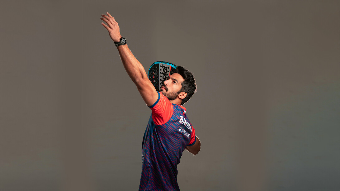Athletic padel player getting into position for a shot on an indoor glass court