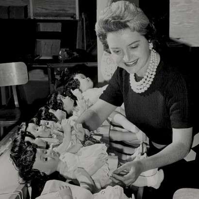 Ruth Handler, executiva da empresa Mattel Toy, posando com coleção de bonecas Barbie, 1961. Explore a dualidade dos papéis femininos na mídia, entre progressismo e valores tradicionais, ao longo das últimas décadas