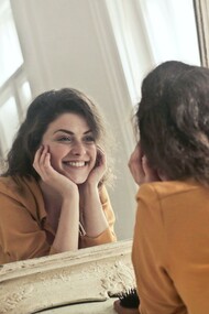 A woman smiling at herself in the mirror, smiling is a cause of happiness in your life