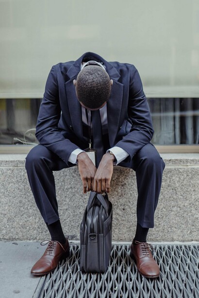 Sentado diante do edifício corporativo, o homem encara o vazio com o crachá ainda pendurado ao peito. Algumas despedidas profissionais acontecem muito antes de alguém abandonar o prédio. O trabalho muda rapidamente de mãos; o tempo perdido, esse não regressa