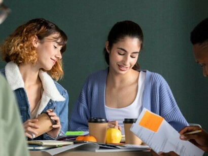 A young man shares and explains his notes with classmates during a study session in a diverse university setting