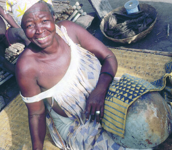Ill. 1. Tonguoy Diarra pausing during the painting of the sleeve of a man’s tunic. The sleeve bearing the “Piece of a gourd” (Filen koloni) pattern is stretched across an empty calabash. Dyers always use the calabash as a support because it enables them to hold the metal spatula vertical to the cloth and to work on very small areas without staining other sections of the design. Kolokani.  
Photocredit Sarah C. Brett–Smith  
