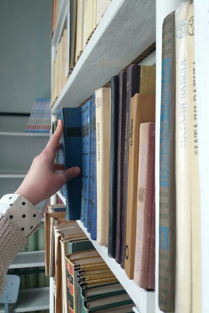 Mano che seleziona un libro che sporge leggermente da uno scaffale