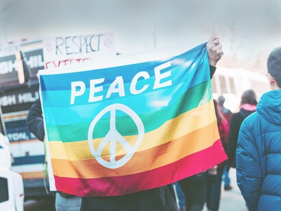 A rainbow-colored flag held high with "peace" written on the back of it along with its symbol to illustrate that the culture of peace is present