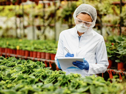 In a modern greenhouse, a female scientist examines potted flowers and records her observations, showcasing advances in plant science and biotechnology innovation