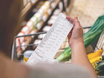 A woman shops at a convenience store and checks her receipt, reflecting the rising cost of living and economic hardship faced by struggling families in the USA