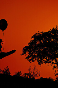 An illusion of a woman holding a balloon on the hand of a man during a sunset as he looks at her with awe at her confidence