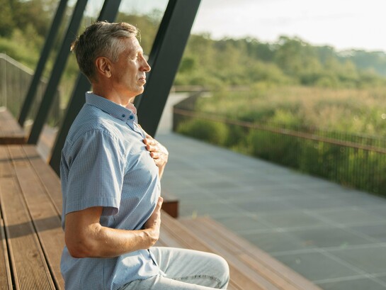 An older man resting one hand on his chest and the other on his abdomen as he breathes deeply, symbolizing awareness of the body's natural rhythm