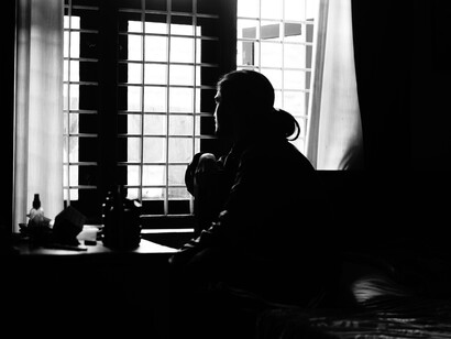 Une photo en noir et blanc d'une personne assise devant une fenêtre
