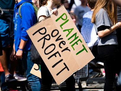 A woman carrying a cardboard sign that reads "planet over profit" which demonstrates that she is not in denial of climate change