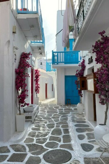 Rows of whitewashed houses with blue shutters sit vacant on a Greek island, symbols of a growing housing crisis and displacement