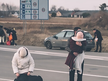 A family on the side of a road next to a luggage bag, escaping from Ukraine