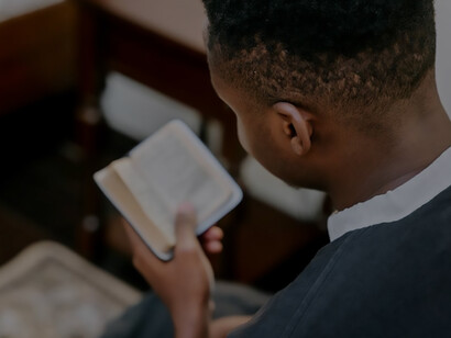 A man clad in a black soutane, solemnly holding a Bible
