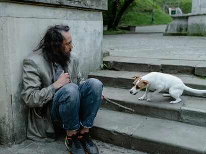 In the USA, a homeless man in blue denim jeans sits beside a white short coat left on the ground