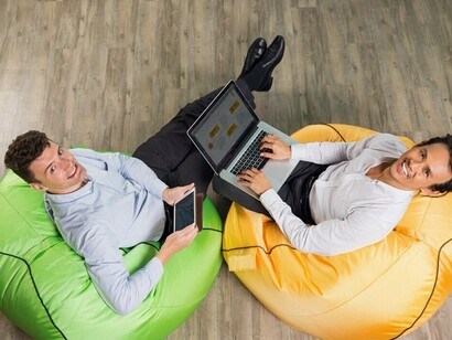 Two businessmen are collaborating using a tablet and laptop, discussing networking platforms, global connectivity, group guidelines, and social media interactions