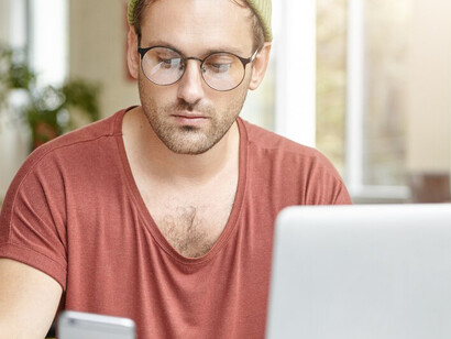 Young man working on laptop in a cafe while checking his phone