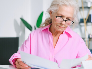 An elderly woman carefully reviewing paperwork, representing the financial uncertainty faced by many pensioners