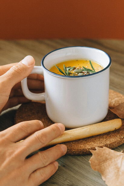 A white ceramic mug filled with hot winter soup, garnished with fresh green herbs