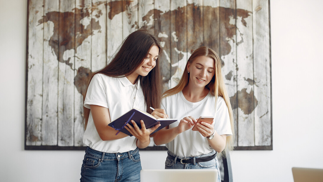 Two exchange language students in white T-shirts working in an office in front of a world map