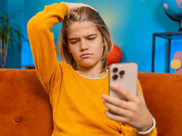 Teenage girl feeling frustrated after losing an online game on her smartphone, overwhelmed by constant notifications while sitting on a sofa at home