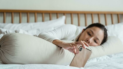 An Asian woman lying in bed while using her smartphone