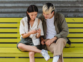A couple sitting outside, looking at the screen of a phone, enjoying the pleasures that social media has to offer