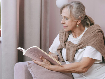 Senior woman wearing glasses enjoying leisure reading on a comfortable sofa indoors