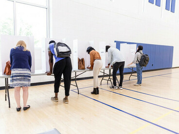 Pessoas diversas votando em cabines reservadas, vistas por trás
