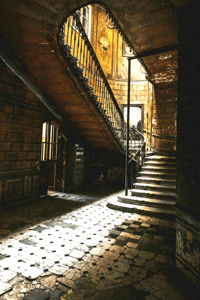 A dark, decaying interior, where broken tiles fracture the floor at the foot of a narrow staircase