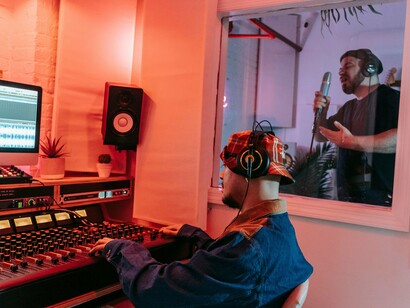 Produtor musical acompanha a gravação enquanto o cantor se apresenta do outro lado do vidro do estúdio. A tecnologia integra o processo, mas não substitui a intenção de quem cria