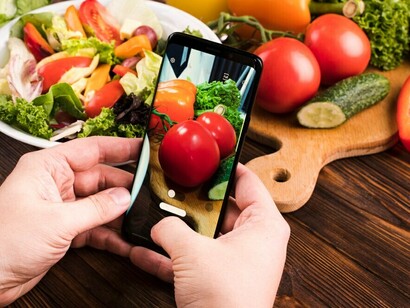 A person using a smartphone to photograph fresh vegetables, integrating AI-driven meal planning and personalized nutrition based on DNA and genomic analysis
