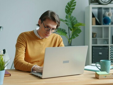 Um homem trabalha concentrado diante de um laptop, sentado à mesa em um ambiente de escritório. A cena traduz a rotina de produtividade contínua descrita no artigo, na qual trabalhar, produzir e entregar podem se sobrepor ao descanso e ao contato com os próprios afetos. A exigência de permanecer produtivo transforma o cotidiano em uma sequência de atividades que nem sempre deixa espaço para sentir, elaborar ou simplesmente interromper o ritmo