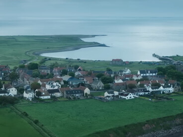 A quiet coastal village surrounded by green fields, symbolizing humanity’s determination to rebuild after catastrophe