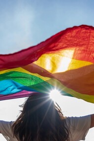  A young woman waving LGBTQIA+ flag under the sky