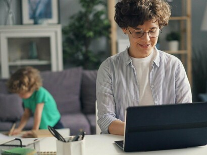 A mother managing her workload while her child plays in the background, symbolising the balance between attention and independence