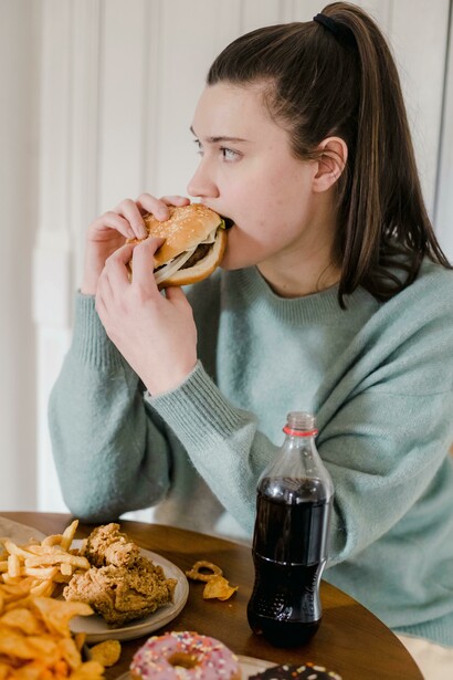 A woman enjoying fried chicken and a hamburger at a table, illustrating the appeal of ultra-processed foods and junk food addiction
