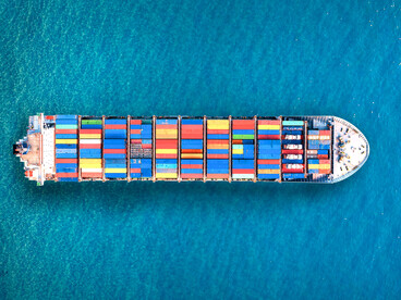 An aerial view of a cargo ship sailing through the ocean, symbolising the flow of goods sustaining global economies
