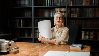 Une femme âgée montrant un livret alors qu'elle est assise dans une bibliothèque