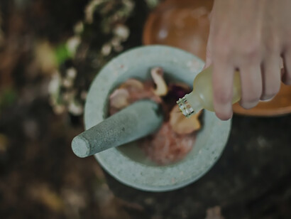 Person pouring liquid from bottle inside mortar and pestle