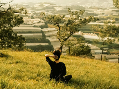 A person sitting quietly on a hill, looking out over the city, resting and deep in thought
