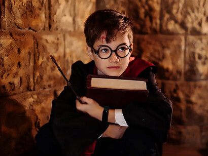 A young wizard enthusiast, sporting black framed eyeglasses and donned in a meticulously detailed Harry Potter costume, adds an authentic touch to his ensemble as he enchantingly holds a wizarding book