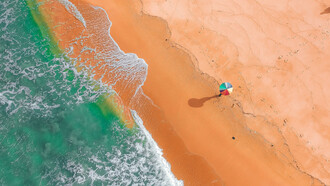 Pessoa passeia pela areia da praia com guarda-sol colorido