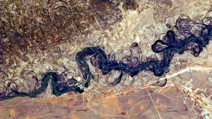 The Syr Darya River floodplain appears here as a maze of winding meanders and loops at the image’s center. The darkest areas mark dense brush along the river’s current course, filled with blue-green water, while lighter wisps of vegetation trace the swampy depressions, or sloughs, that flank it