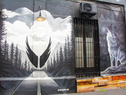 Mural de alas en color negro con una carretera de fondo por la artista Juli Bussot. Palermo, Buenos Aires, Argentina