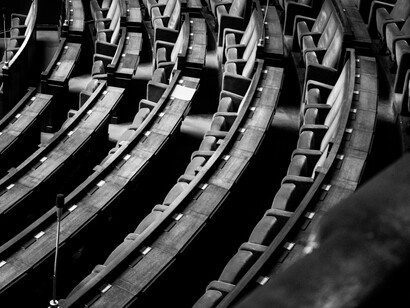 Toma en blanco y negro en ángulo picado que muestra la disposición curva e inclinada de las filas de asientos vacíos en un auditorio o parlamento
