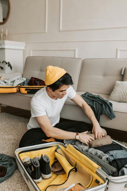 Travel blogger packing his clothes while listening to music on headphones