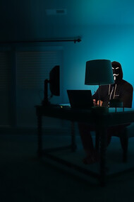 A man at a computer disguised as an anonymous hacker wearing a Guy Fawkes mask.