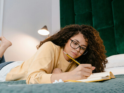 A girl lying on a bed while writing in a notebook