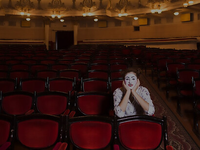 In the serene ambiance of an auditorium, a female mime sits absorbed in reading a manuscript, evoking a scene of artistic contemplation and solitude