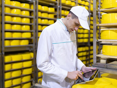 A technologist, laptop in hand, oversees the dairy factory's production line, implementing solutions for efficient food supply chain management, enhancing food traceability, and leveraging blockchain technology